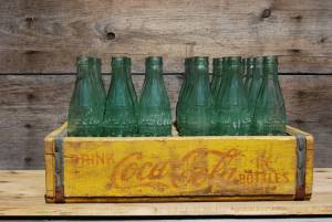  After 1937 and through the '40s Coca-Cola was in a green-tinted glass bottle with no colored printing and were delivered in wooden crates / cases (as shown above). Some crates were designed for individual bottles, others had quadrants designed to hold a six-pack in a thin cardboard carrier.